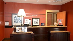 A reception desk with a 'Welcome to Americus' sign, framed pictures, a lamp, and a minibar.