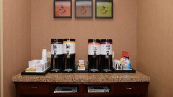 A coffee station with four coffee makers, a stack of disposable cups, and a coffee machine.
