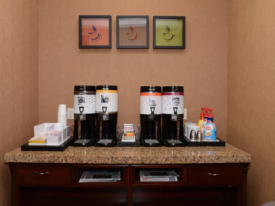 A coffee station with four coffee makers, a stack of disposable cups, and a coffee machine.