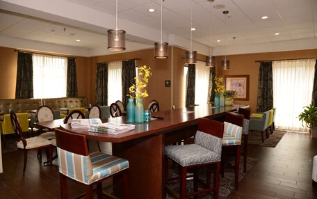 A hotel dining area with a long wooden table, multiple chairs, and hanging pendant lights.