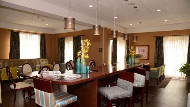 A hotel dining area with a long wooden table, multiple chairs, and hanging pendant lights.