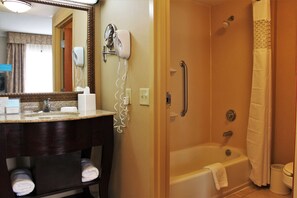 A bathroom with a sink, mirror, hairdryer, and a walk-in shower with a grab bar. - Hampton Inn Americus (Americus)