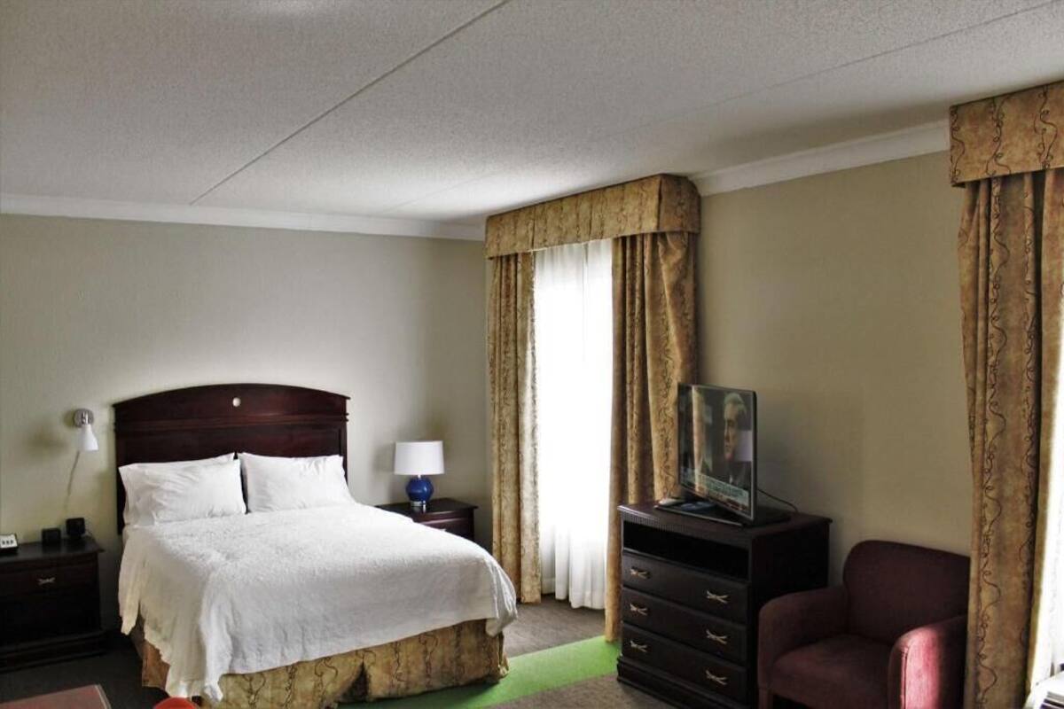 Une chambre d’hôtel avec un lit, une commode, une télévision et des rideaux.