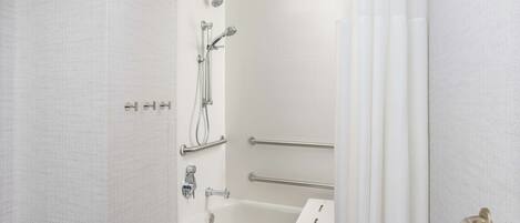 A bathroom with a white bathtub, a shower with a handheld showerhead, and a grab bar.
