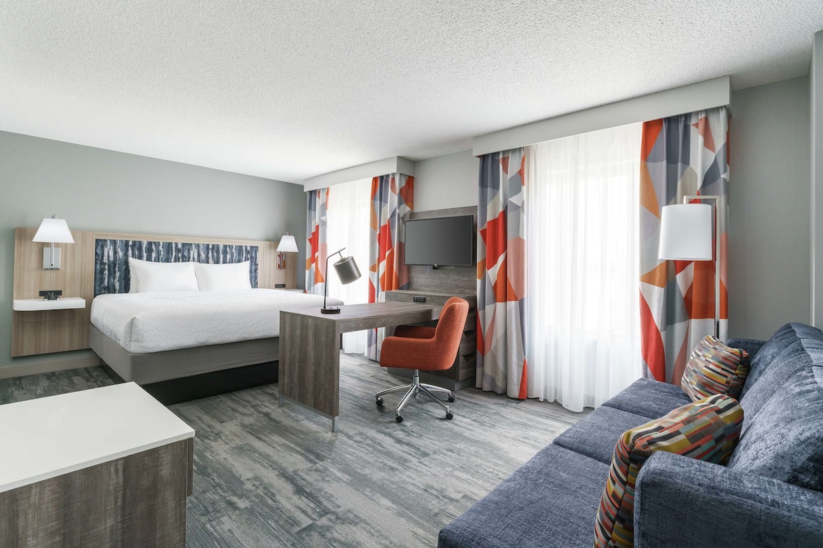Een hotelkamer met een bed, bureau, bureaustoel, bank en een televisie.
