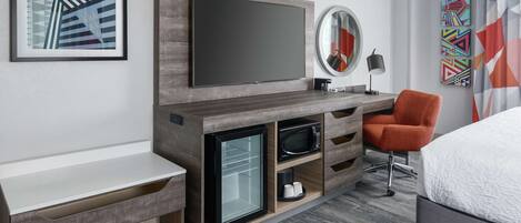 Una habitación de hotel moderna con televisión integrada, un refrigerador miniatura, microondas y una zona de estar con una silla.