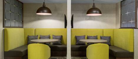 A modern seating area with yellow upholstered benches and round tables, featuring pendant lighting and a decorative wall panel.