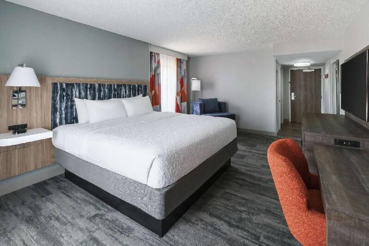 Een hotelkamer met een bed, een bureau, een stoel, een televisie en een deur.