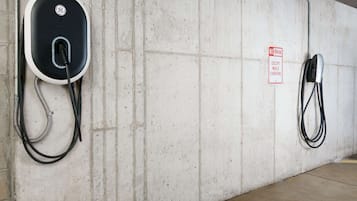 A parking area with electric vehicle charging stations, a concrete wall, and a 'No Parking Except While Charging' sign.