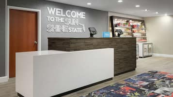 A hotel reception area with a modern design, a welcome sign, a self-service kiosk, and a minibar.