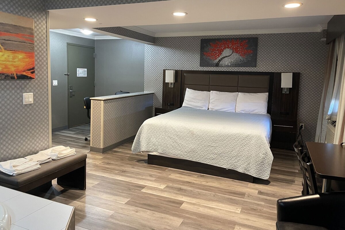 Une chambre d’hôtel avec un lit, des tables de chevet, un bureau, un banc et un tableau au mur.