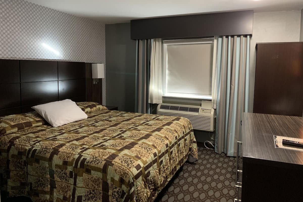 A hotel room with a large bed, a desk, a window with curtains, an air conditioning unit, and a headboard.