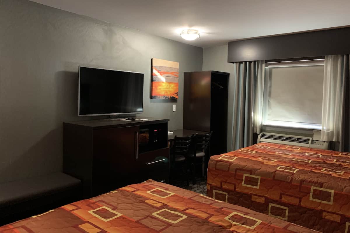 A hotel room with a TV, a desk, two beds, a wardrobe, and a window with curtains.