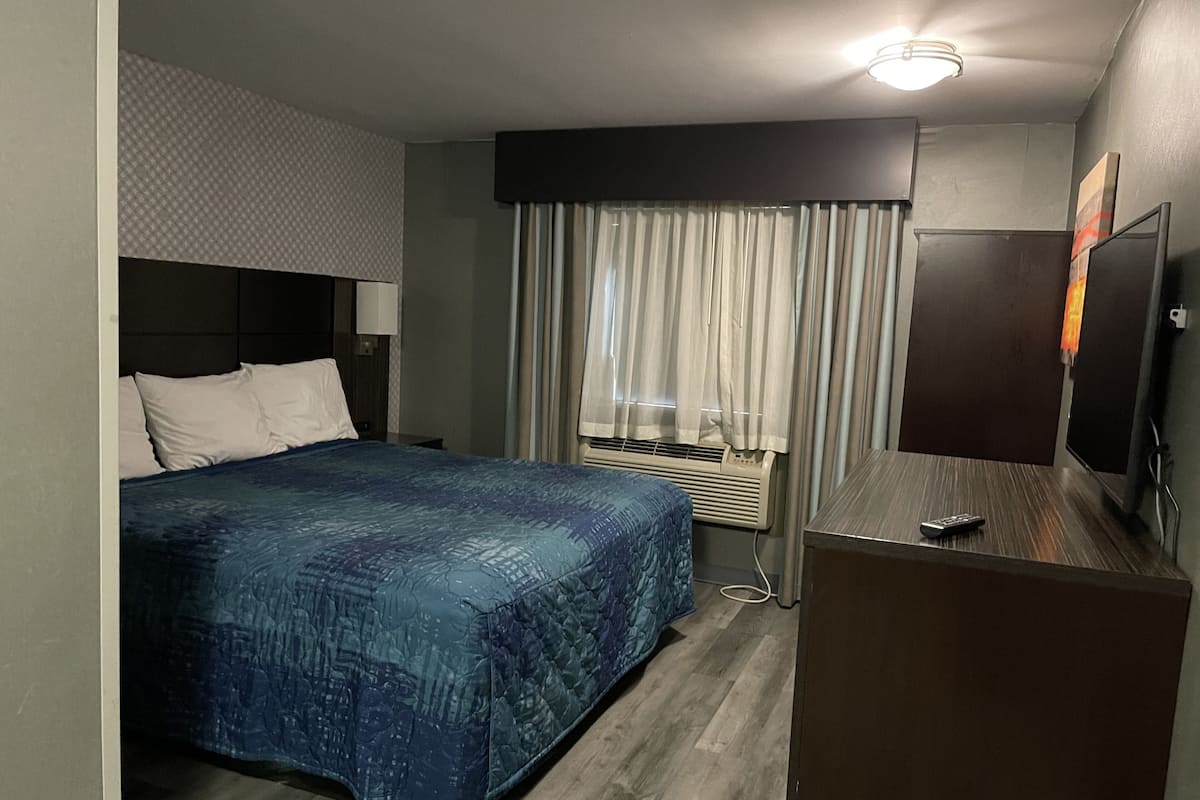 A hotel room with a bed, a desk, a television, and a window with curtains.