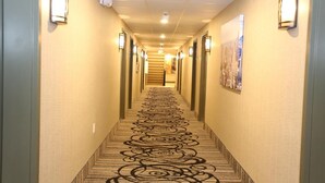 Un pasillo de hotel con alfombra estampada, luces fijadas en la pared y una escalera al final.