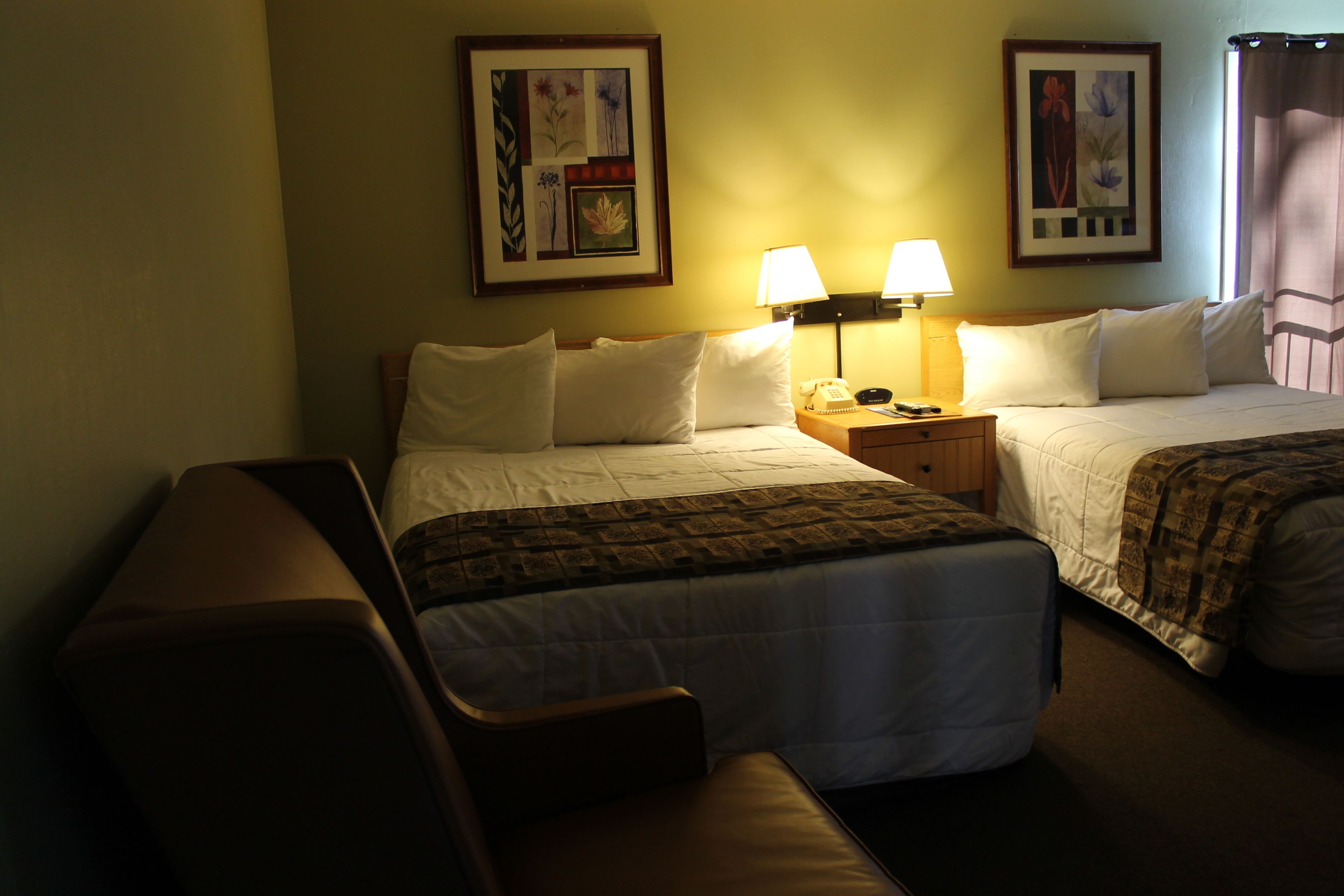 Une chambre d’hôtel avec deux lits, un bureau et une chaise. Il y a deux lampes sur le bureau et un tableau encadré au mur.