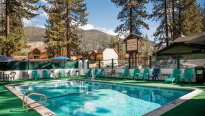 A swimming pool with a diving board, surrounded by green chairs and a mountain backdrop.