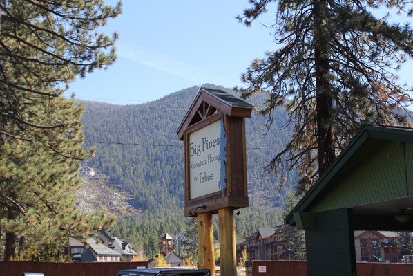 A mountain house sign with a view of a forested mountain and buildings in the background.