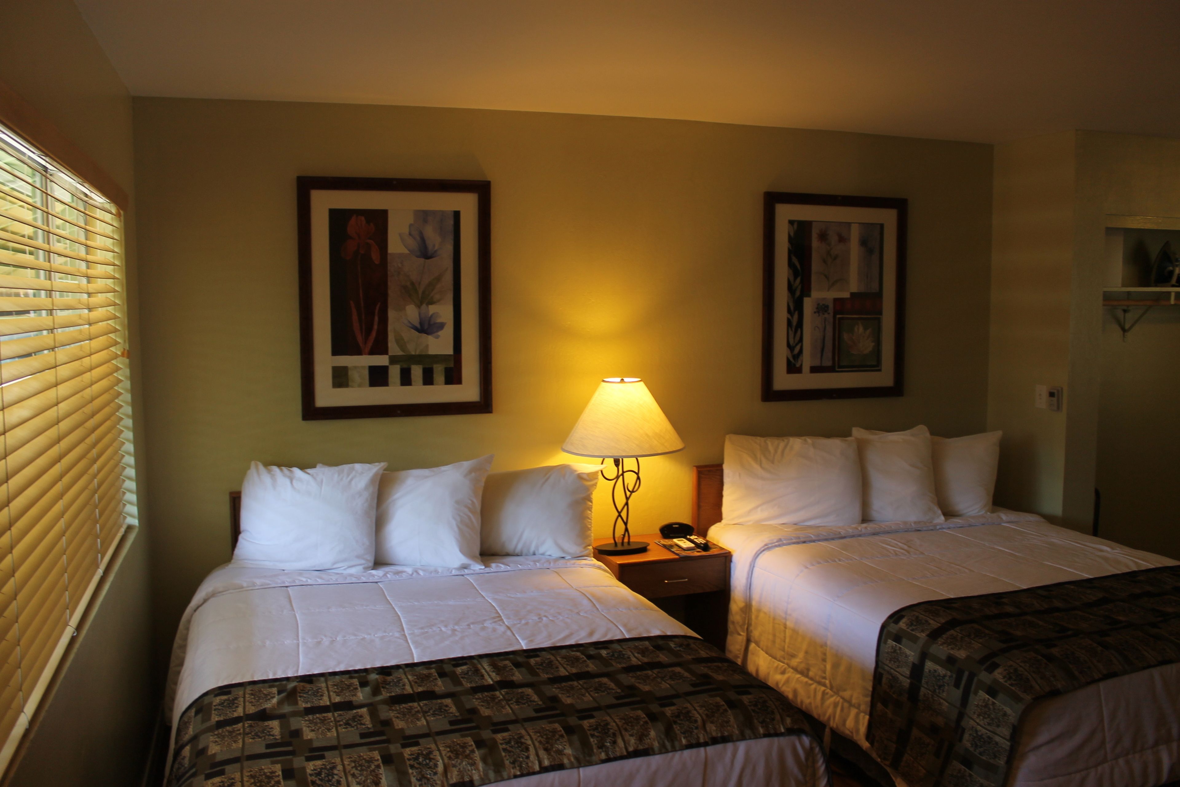 A hotel room with two beds, a nightstand, a lamp, and framed artwork on the walls.