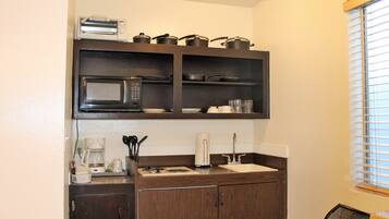 A compact kitchen with a microwave, toaster, and a coffee maker. There are cabinets below and a window with blinds to the right.