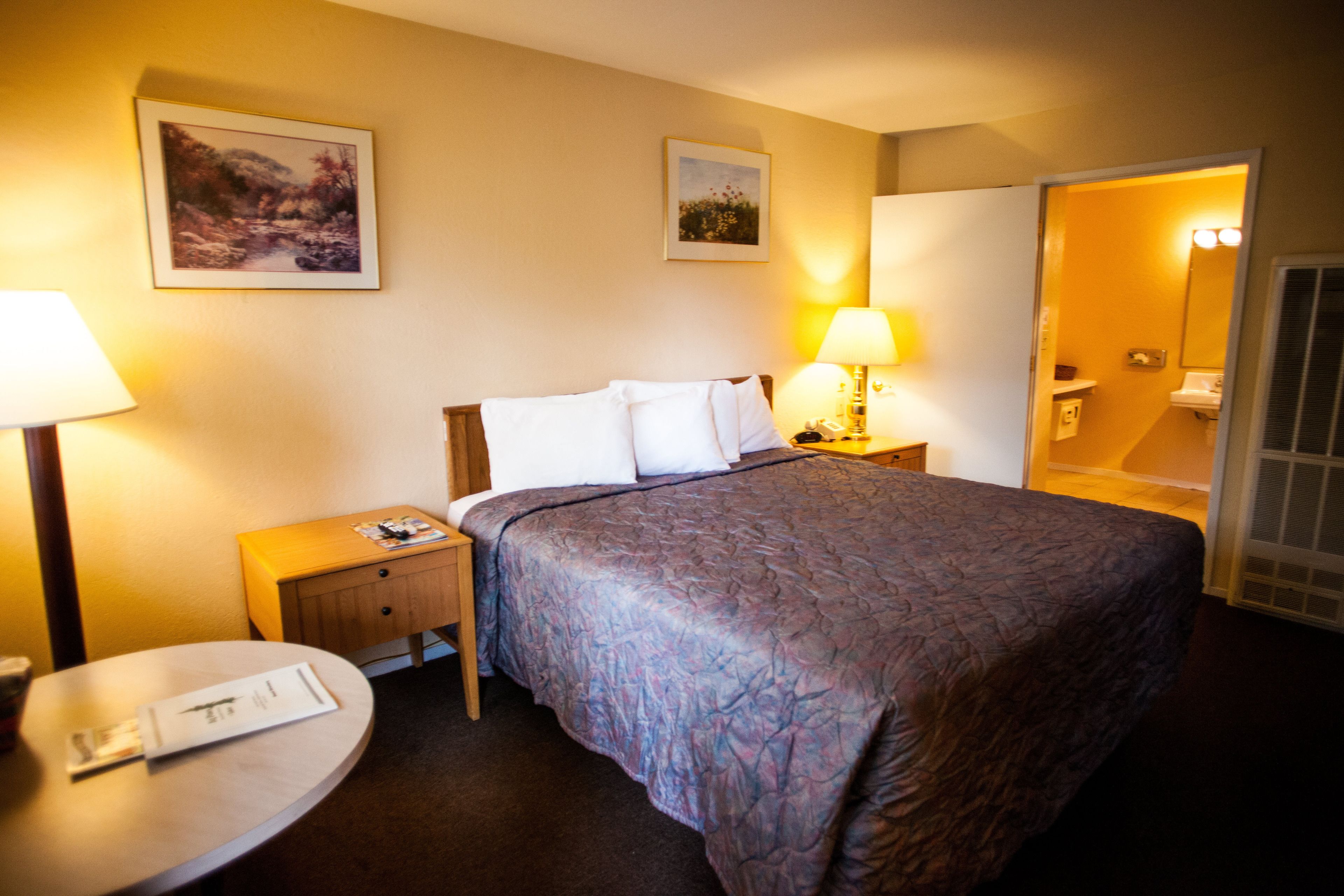 Une chambre d’hôtel avec un grand lit, deux tables de chevet, une table ronde et une salle de bain visible à travers une porte ouverte.