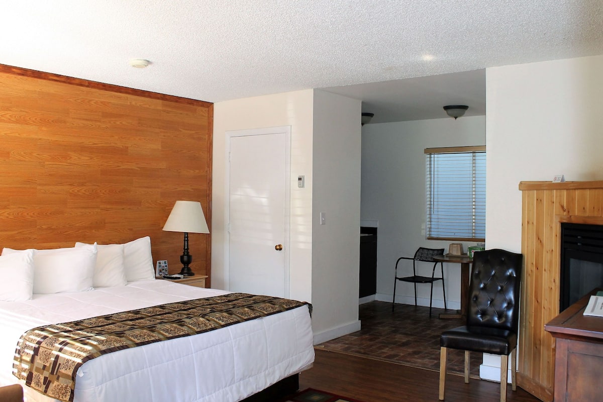 Quarto de hotel com cabeceira de madeira, cama com roupa de cama branca, escrivaninha com cadeira e lareira.