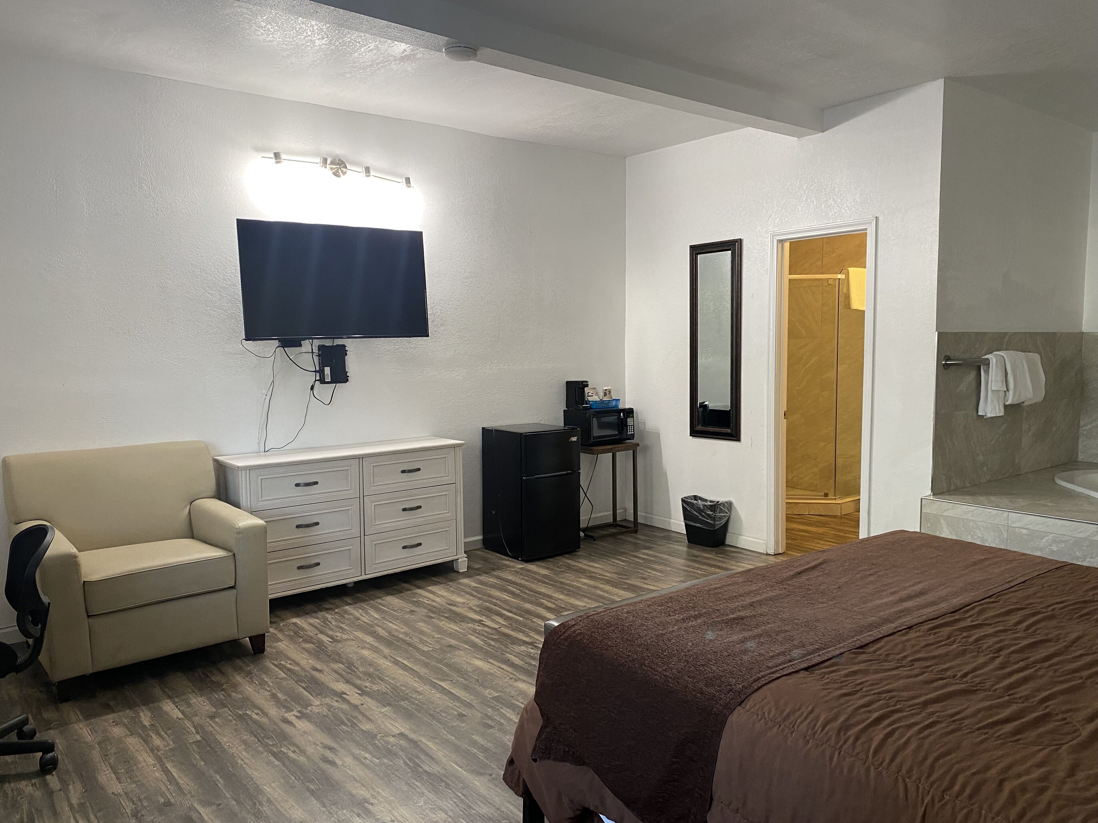 Quarto de hotel com cama, escrivaninha com computador, cadeira, penteadeira, televisão, espelho e banheiro com chuveiro e banheira.