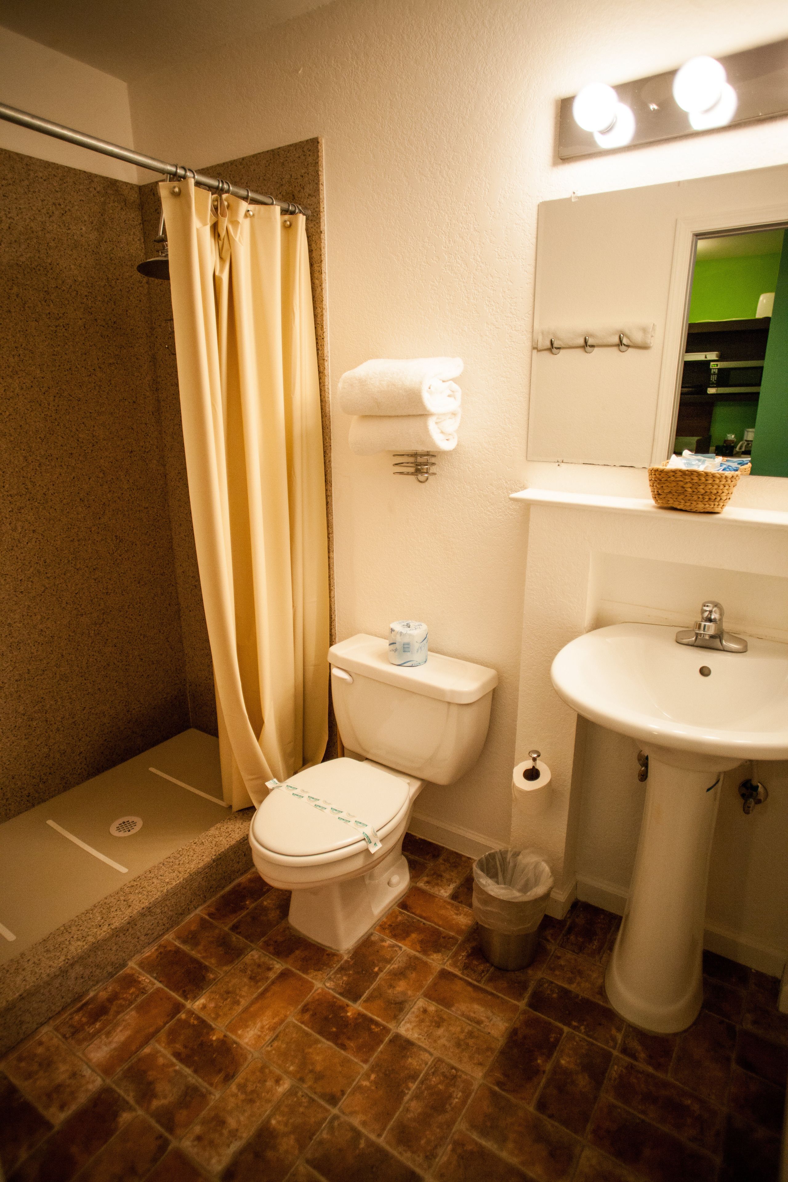 Un baño con ducha, inodoro, lavabo y un espejo con luces arriba.