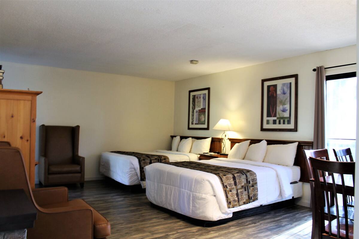 Quarto de hotel com duas camas, uma cadeira de madeira, uma escrivaninha e um abajur.