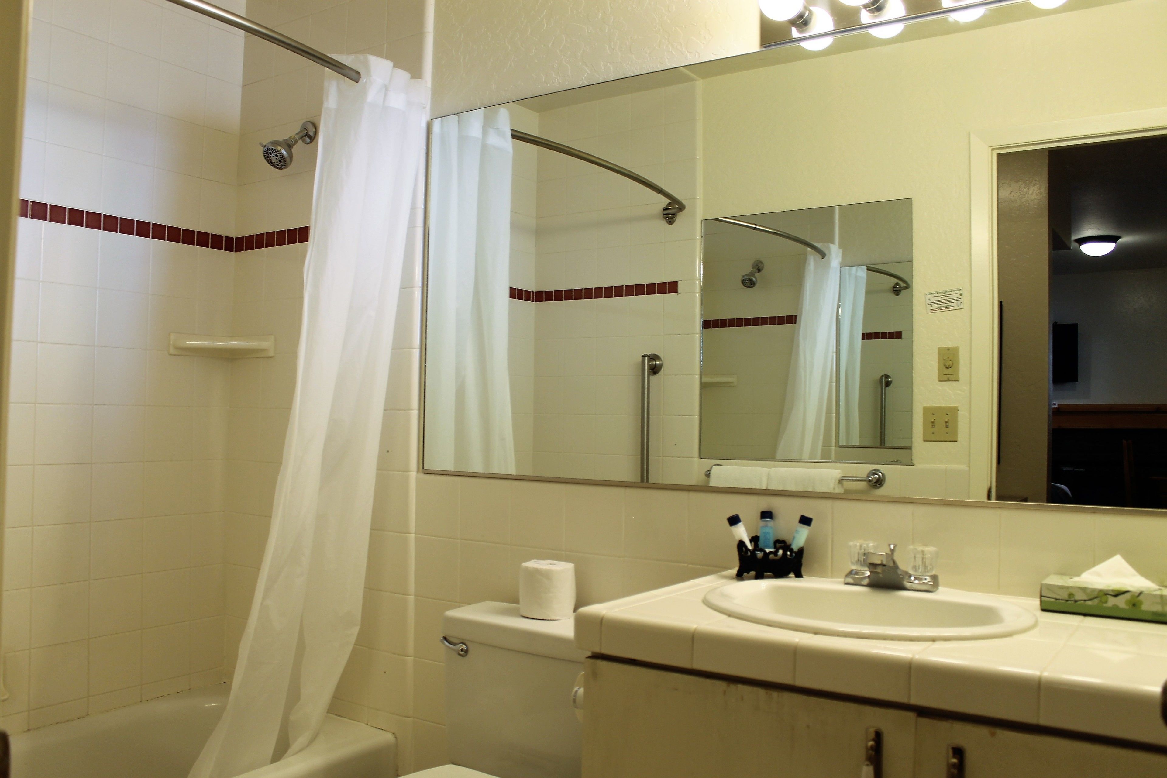 A bathroom with a shower, toilet, sink, and mirror.