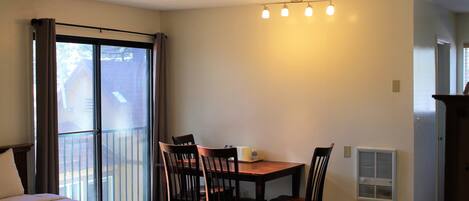A bedroom with a bed, a dining table with chairs, a window with curtains, and a ceiling light fixture.