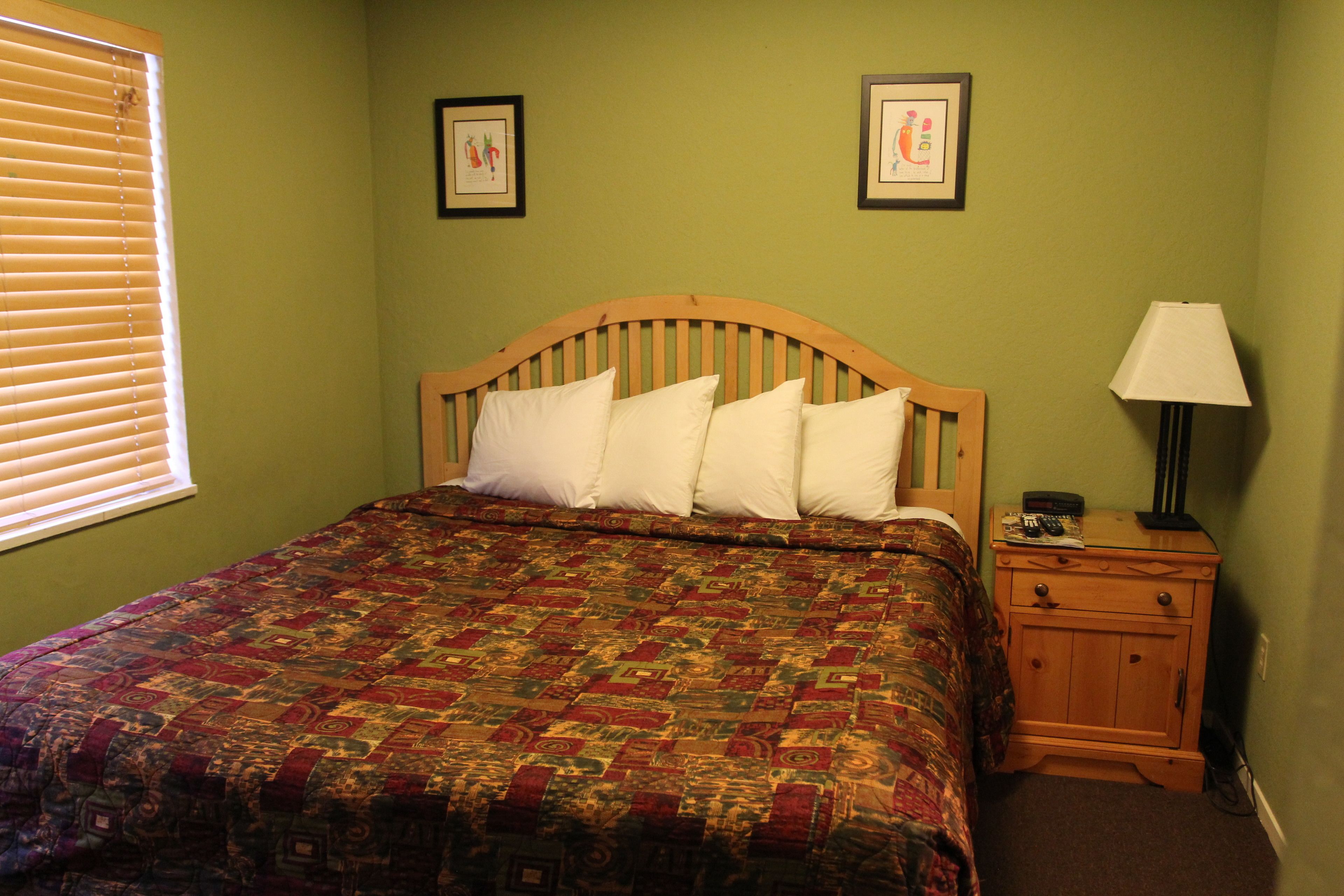 A bedroom with a wooden headboard, a quilted bedspread, a bedside table with a lamp, and two framed pictures on the wall.