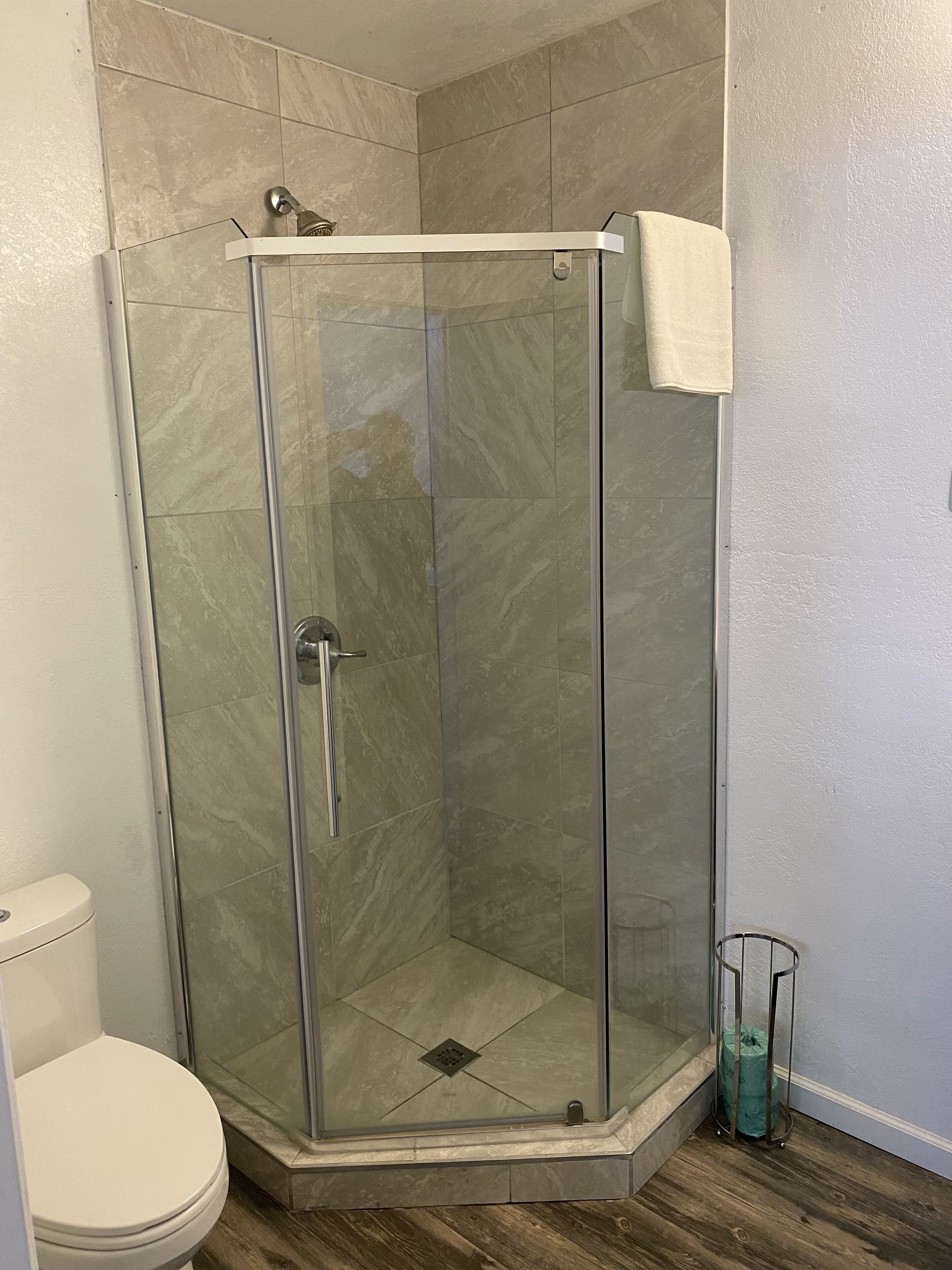 A corner shower with glass doors and a white towel hanging on the wall.