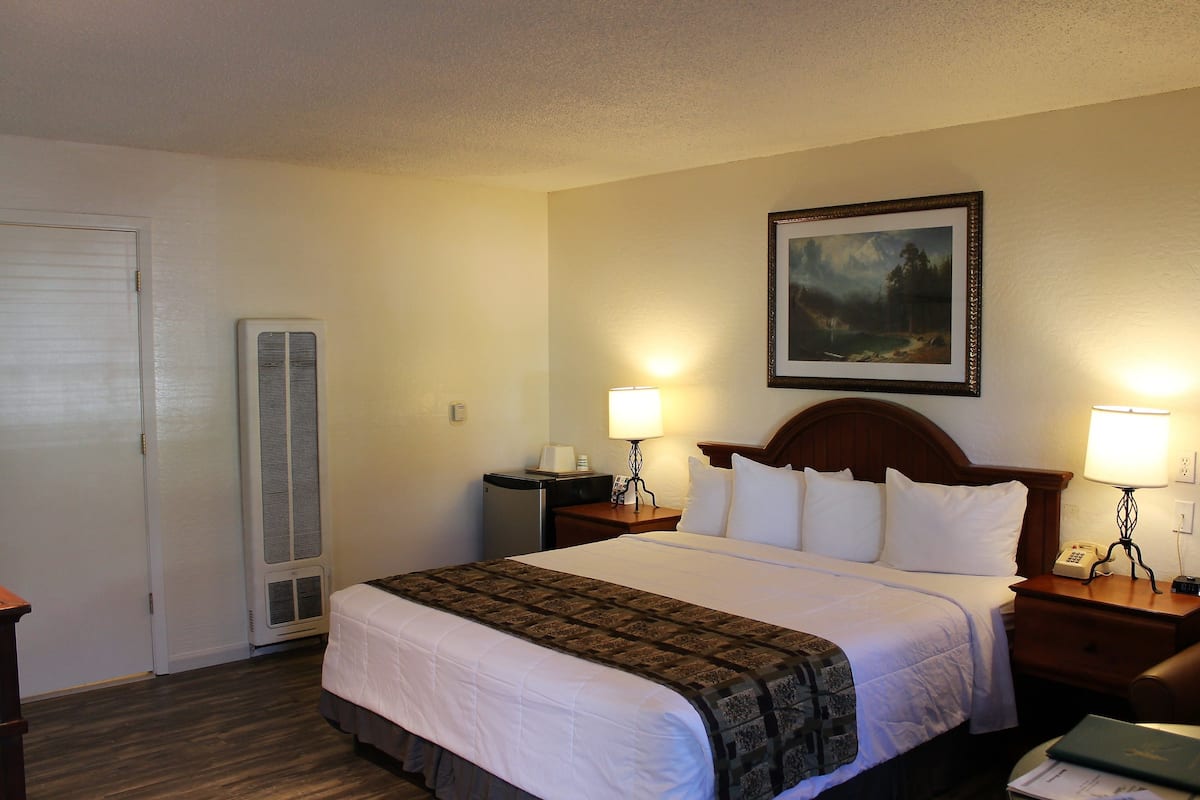 Quarto de hotel com uma cama, duas mesas de cabeceira com luminárias, um quadro na parede e uma porta.