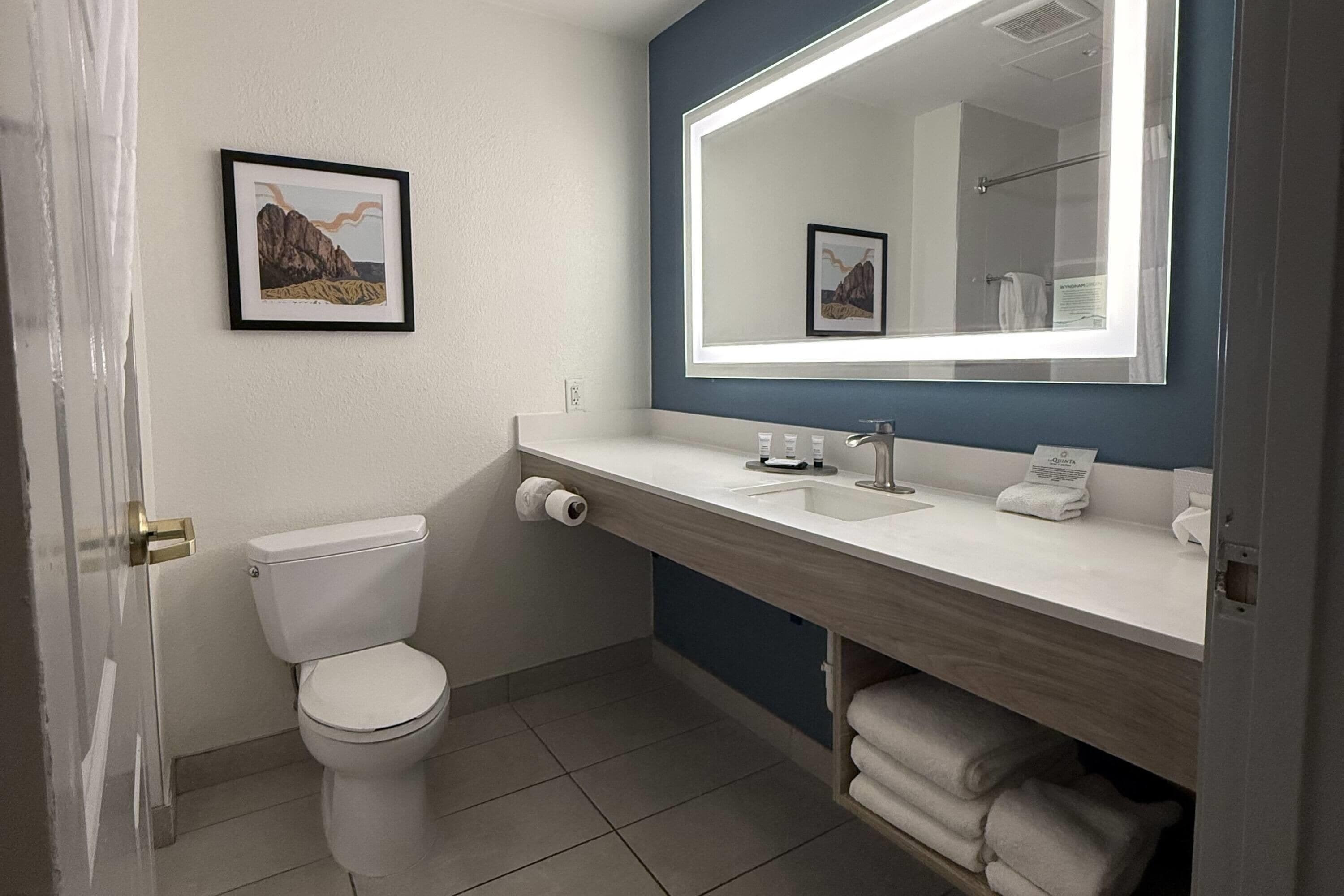 A modern bathroom with a white toilet, a sink with a mirror, and a framed picture on the wall.