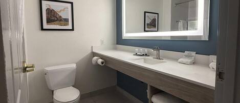A modern bathroom with a white toilet, a sink with a mirror, and a framed picture on the wall.