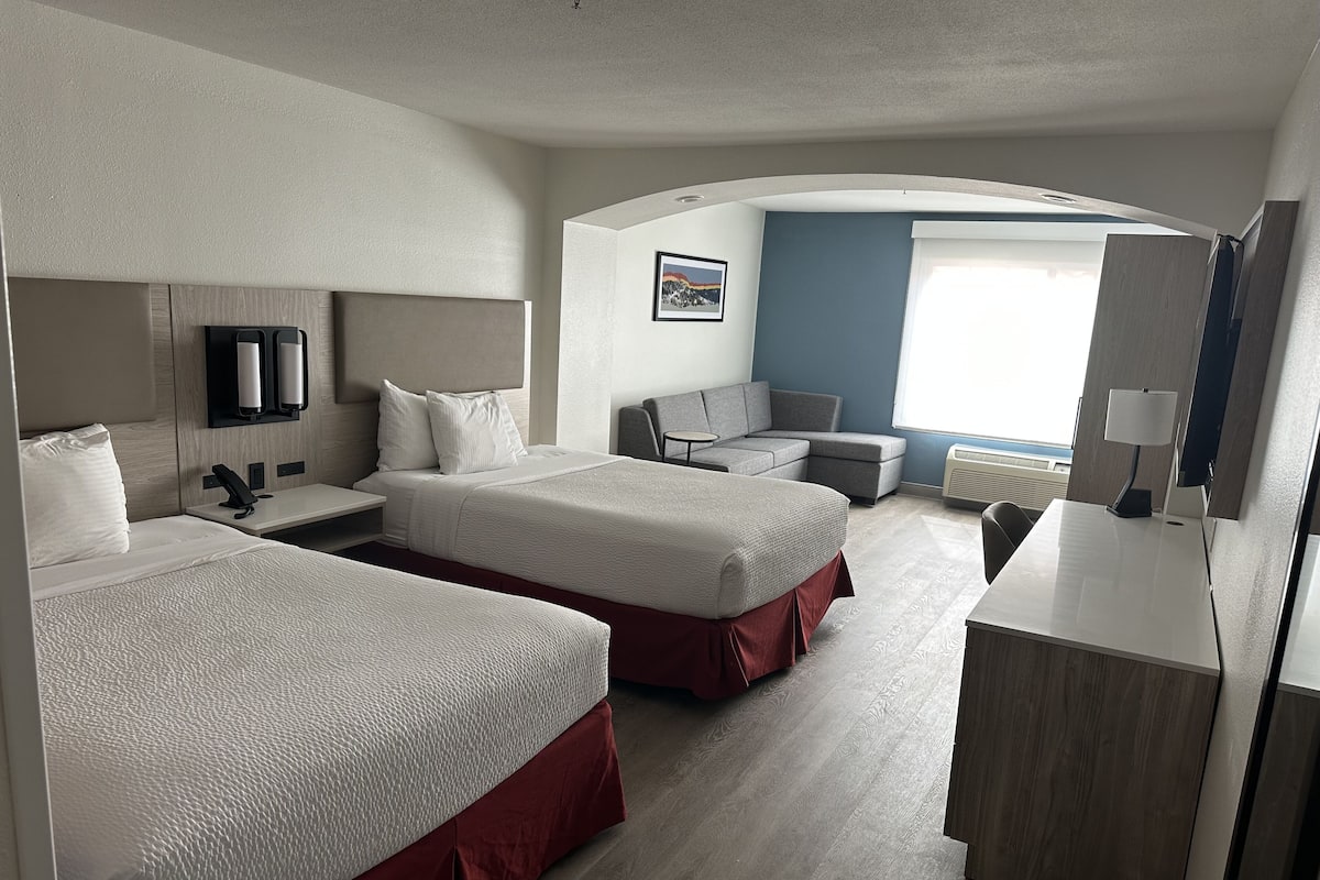 A hotel room with two beds, a desk, a chair, a TV, and a window with a view.
