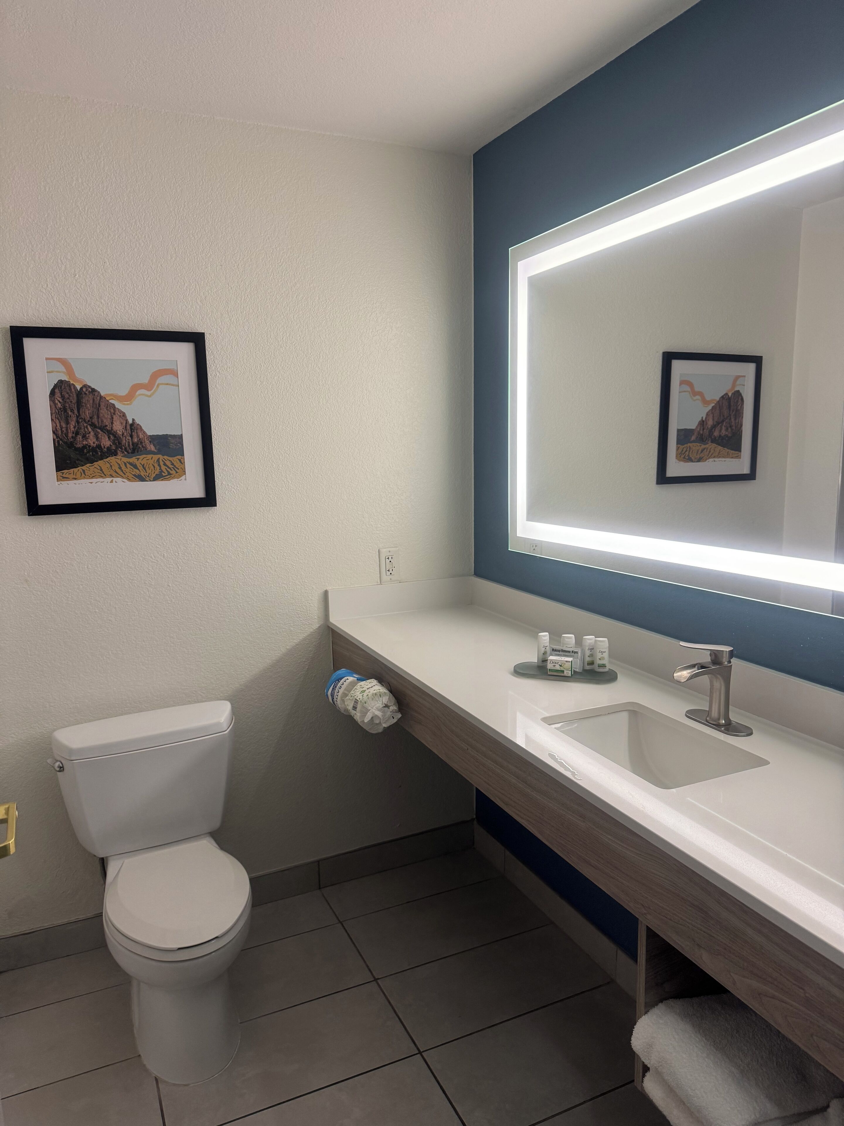 Un baño moderno con inodoro, lavabo y un espejo grande con iluminación integrada.