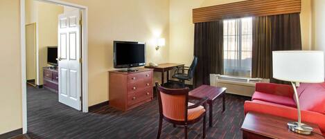 Quarto de hotel com televisão, escrivaninha, cadeira, sofá e luminária.