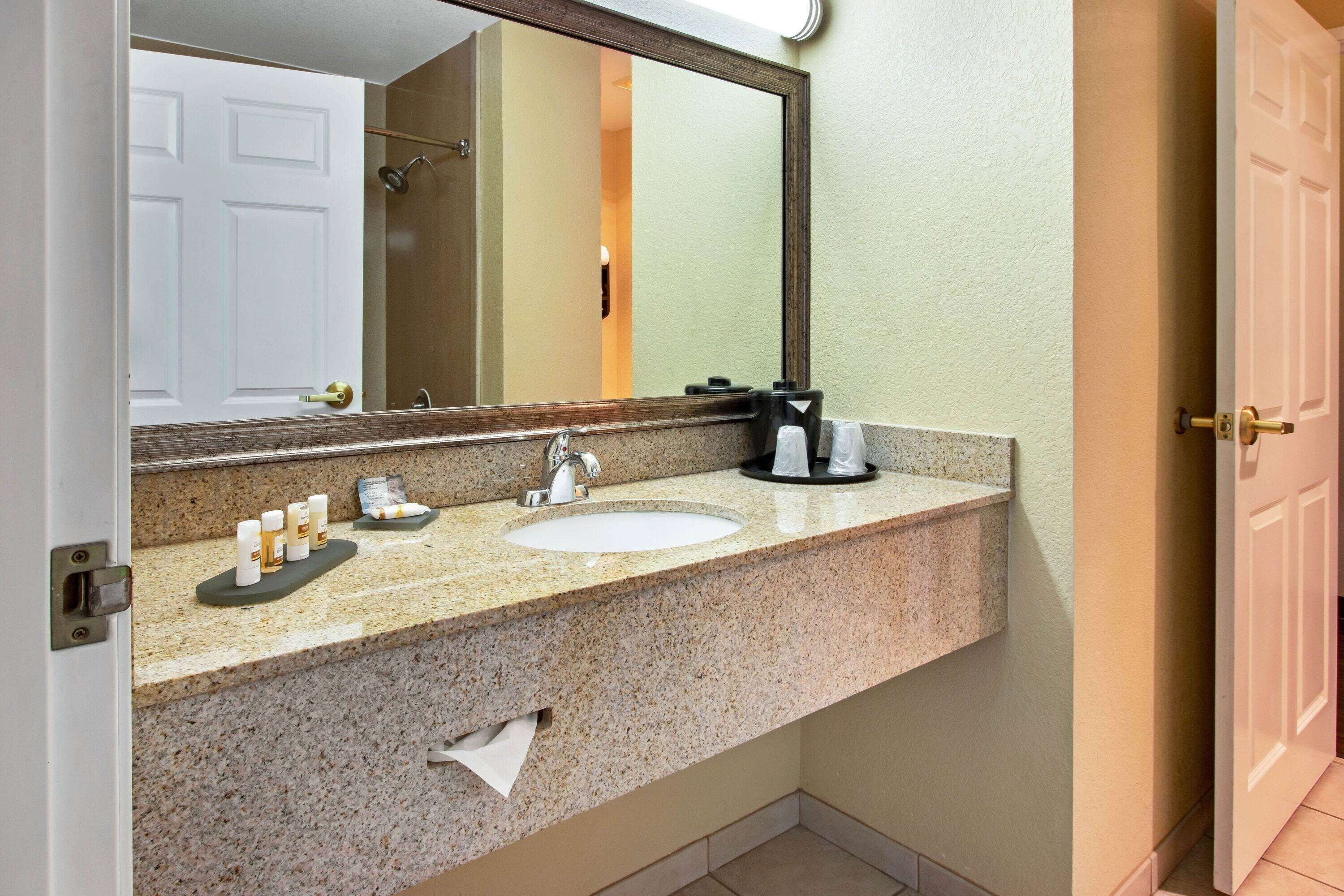 A bathroom with a granite countertop, a white sink, a mirror, and a towel dispenser.