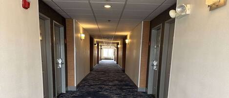 Un pasillo de hotel con pisos alfombrados, puertas a ambos lados e iluminación empotrada en las paredes.