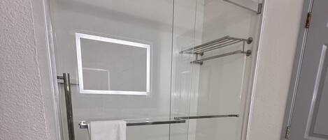Een moderne badkamer met een glazen douchecabine, een zichtbare handdoekhouder en een spiegel.