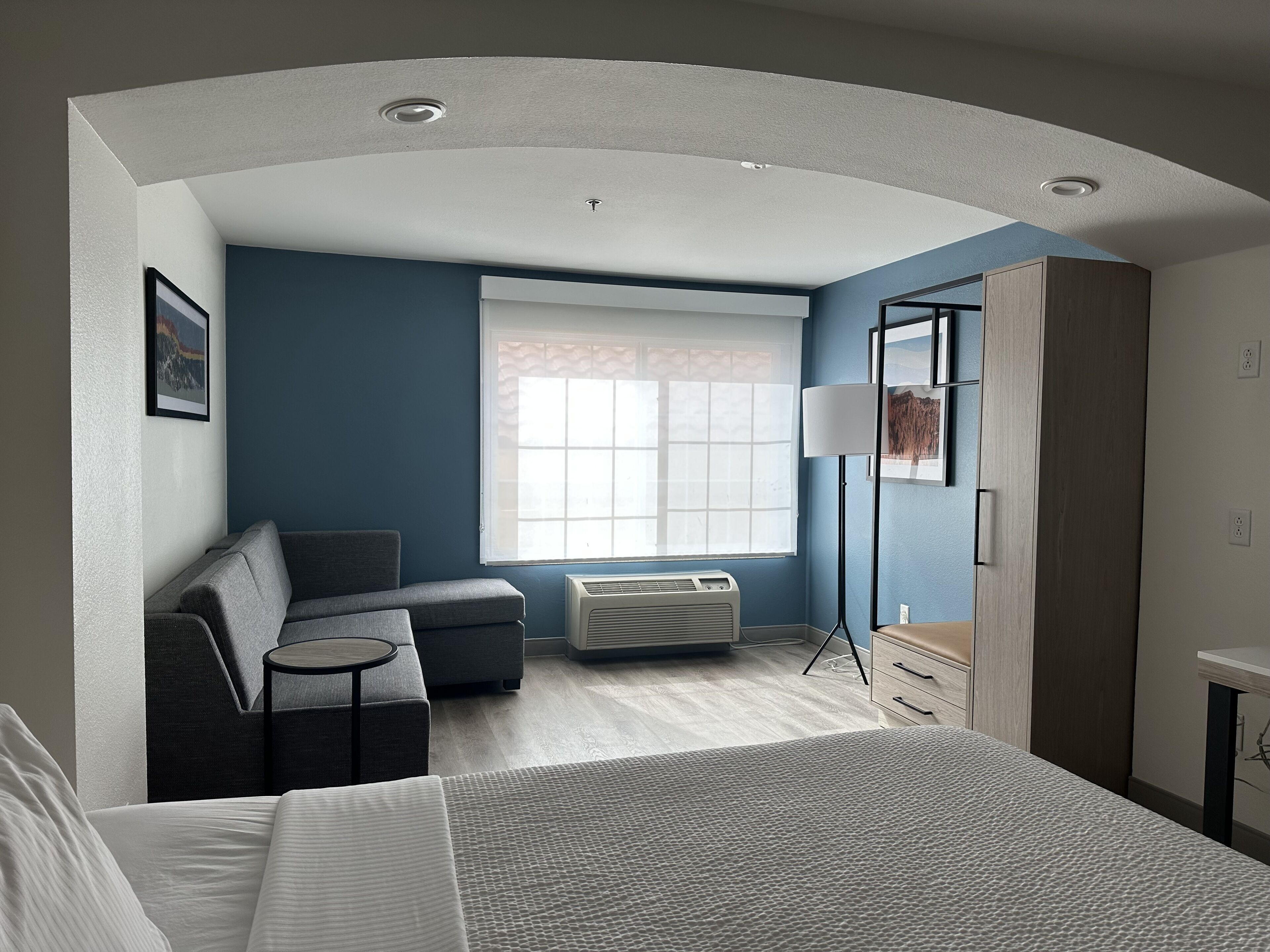 A modern hotel room with a bed, a sofa, a desk, and a wardrobe.
