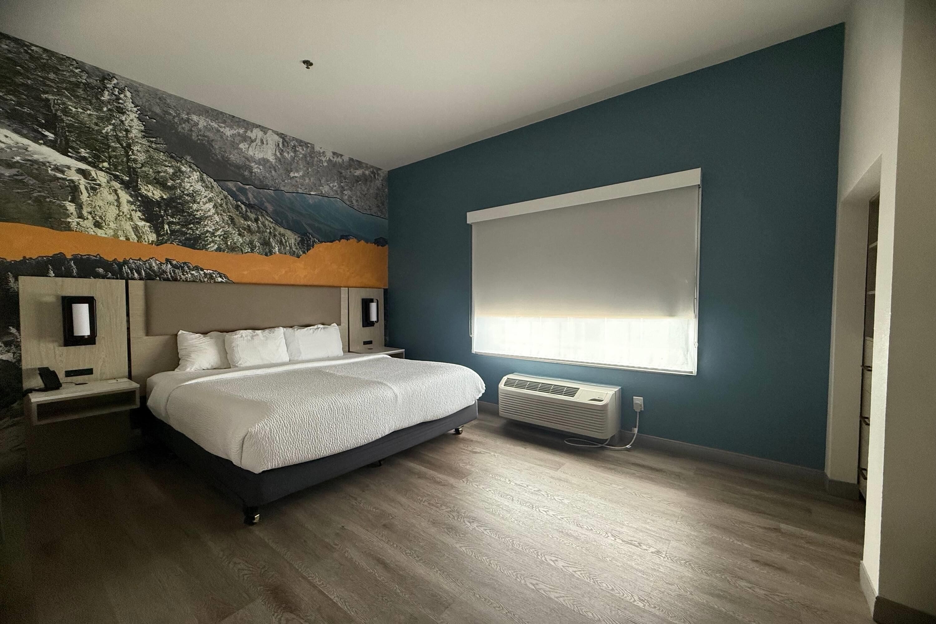 A bedroom with a large bed, a wall-mounted air conditioner, and a window with blinds.
