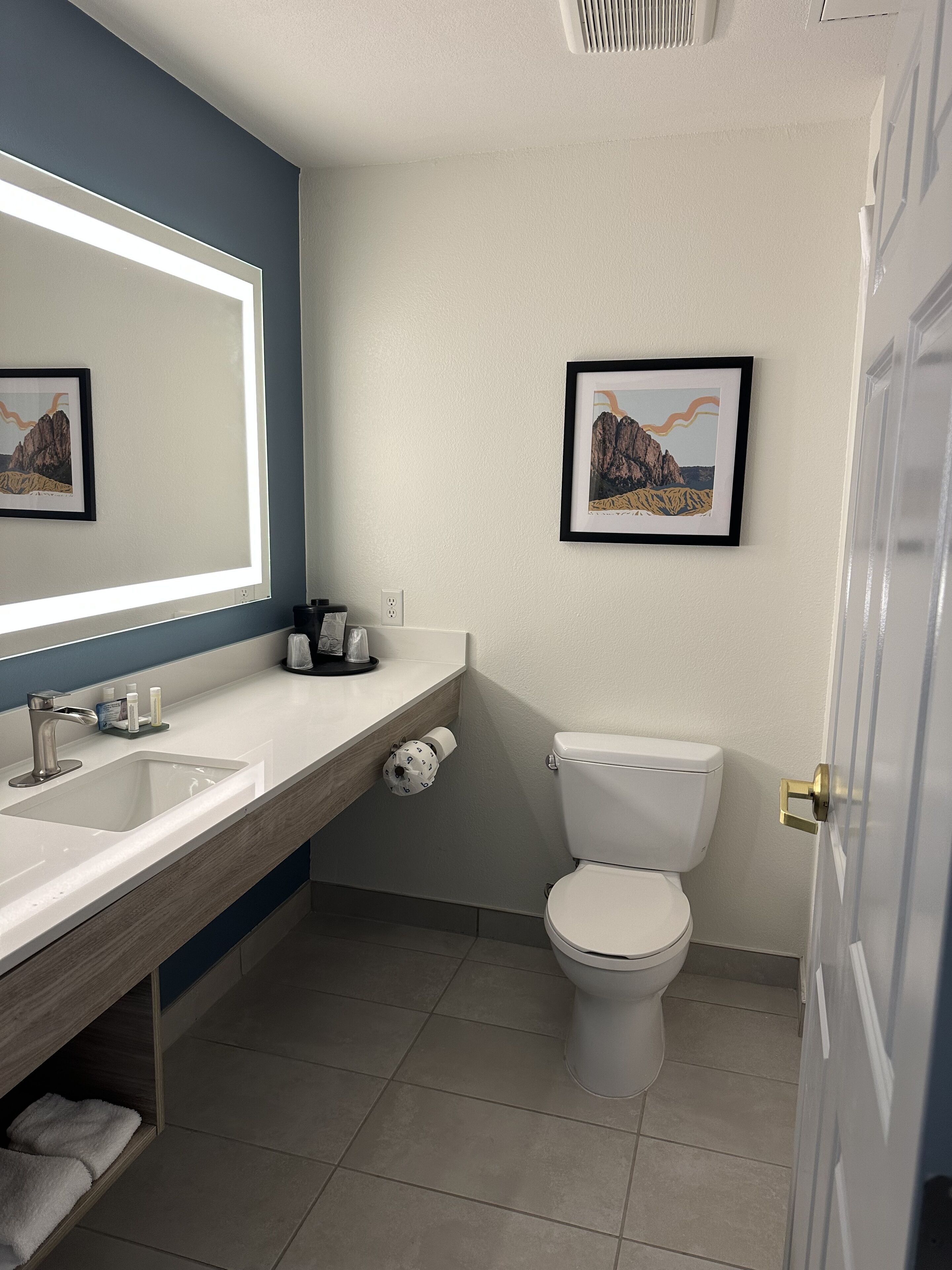 Un baño moderno con un lavamanos blanco, un espejo, un inodoro y una obra de arte enmarcada en la pared.