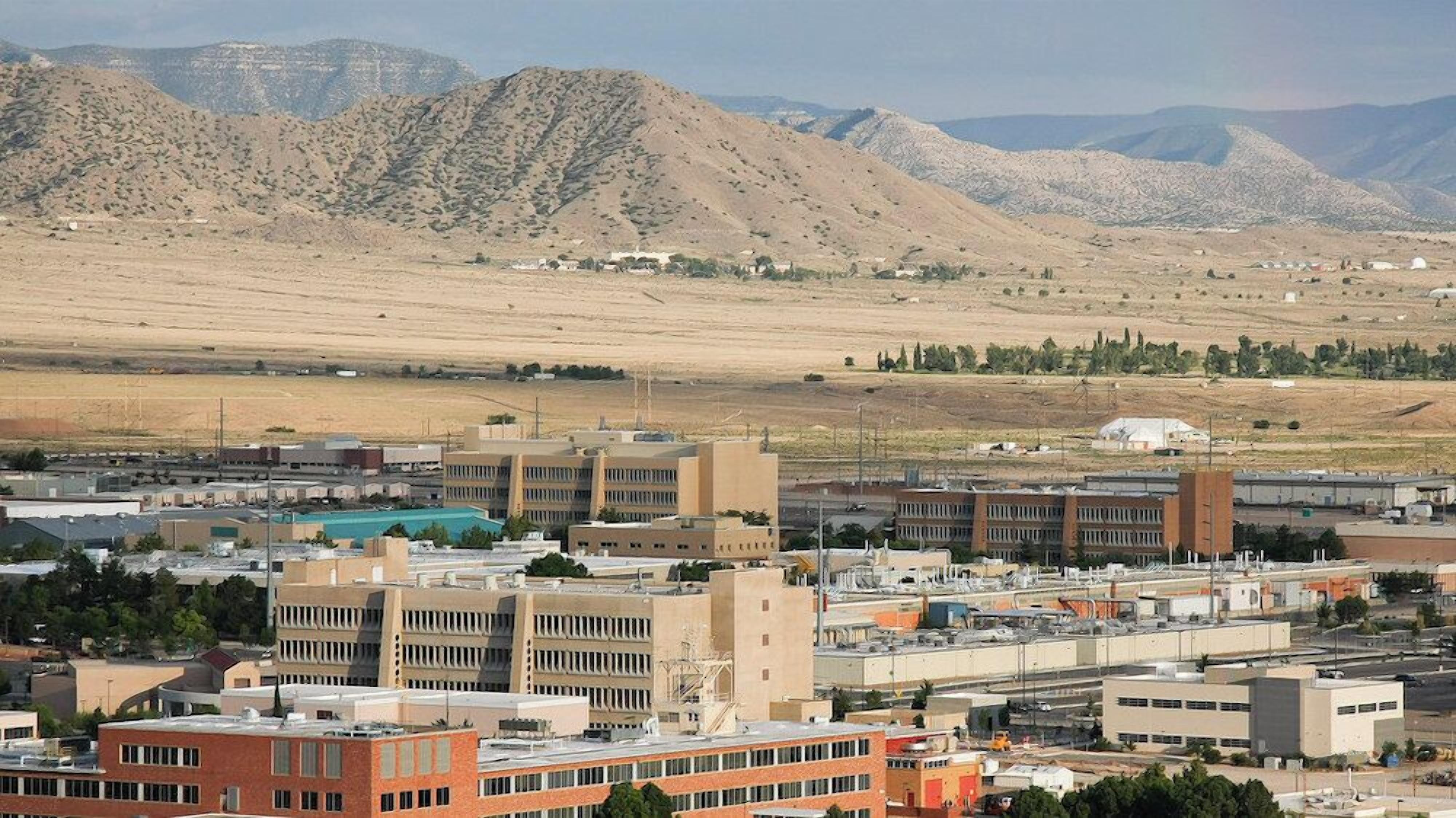 A cityscape with modern buildings, a parking lot, and a mountainous backdrop.