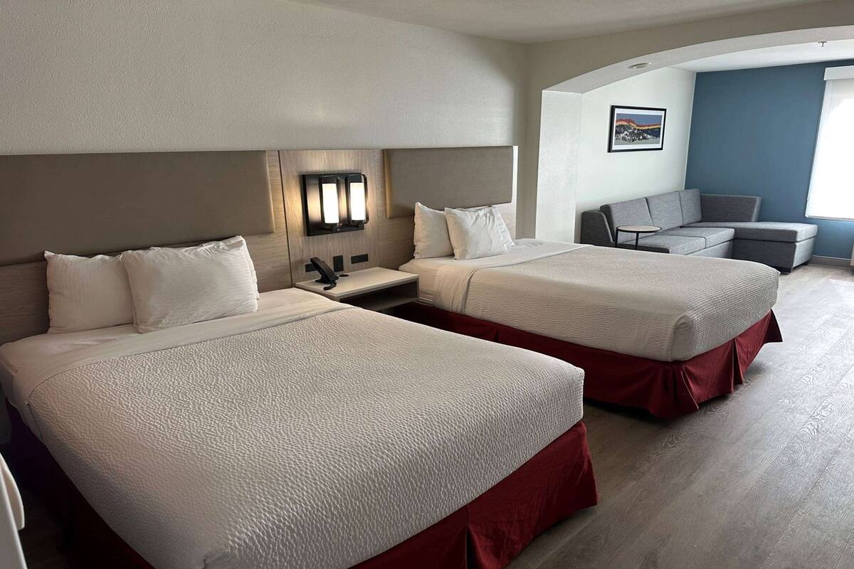 A hotel room with two beds, a desk, and a seating area.