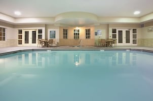Una piscina con borde de baldosas, rodeada de puertas y ventanas, y algunas sillas.