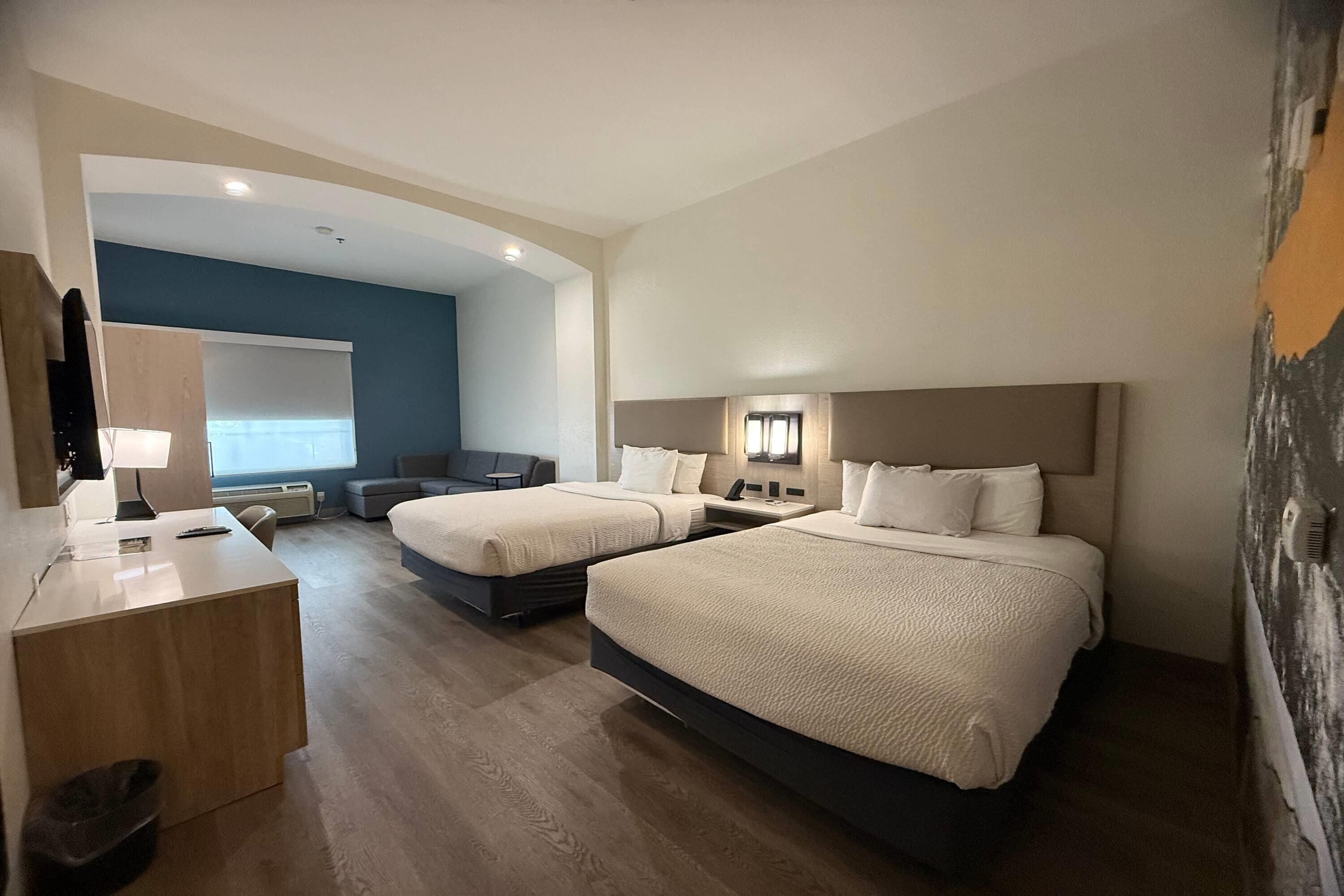 A hotel room with two beds, a desk, a chair, a small sofa, and a large window.
