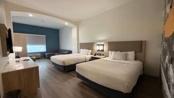 A hotel room with two beds, a desk, a chair, a small sofa, and a large window.